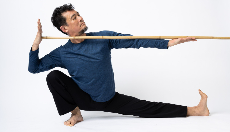 The Sankalpa helps you take aim! Tako holding bamboo in skandasana like they're taking aim. Horizontal orientation. Blue top. Josh Chan photographer